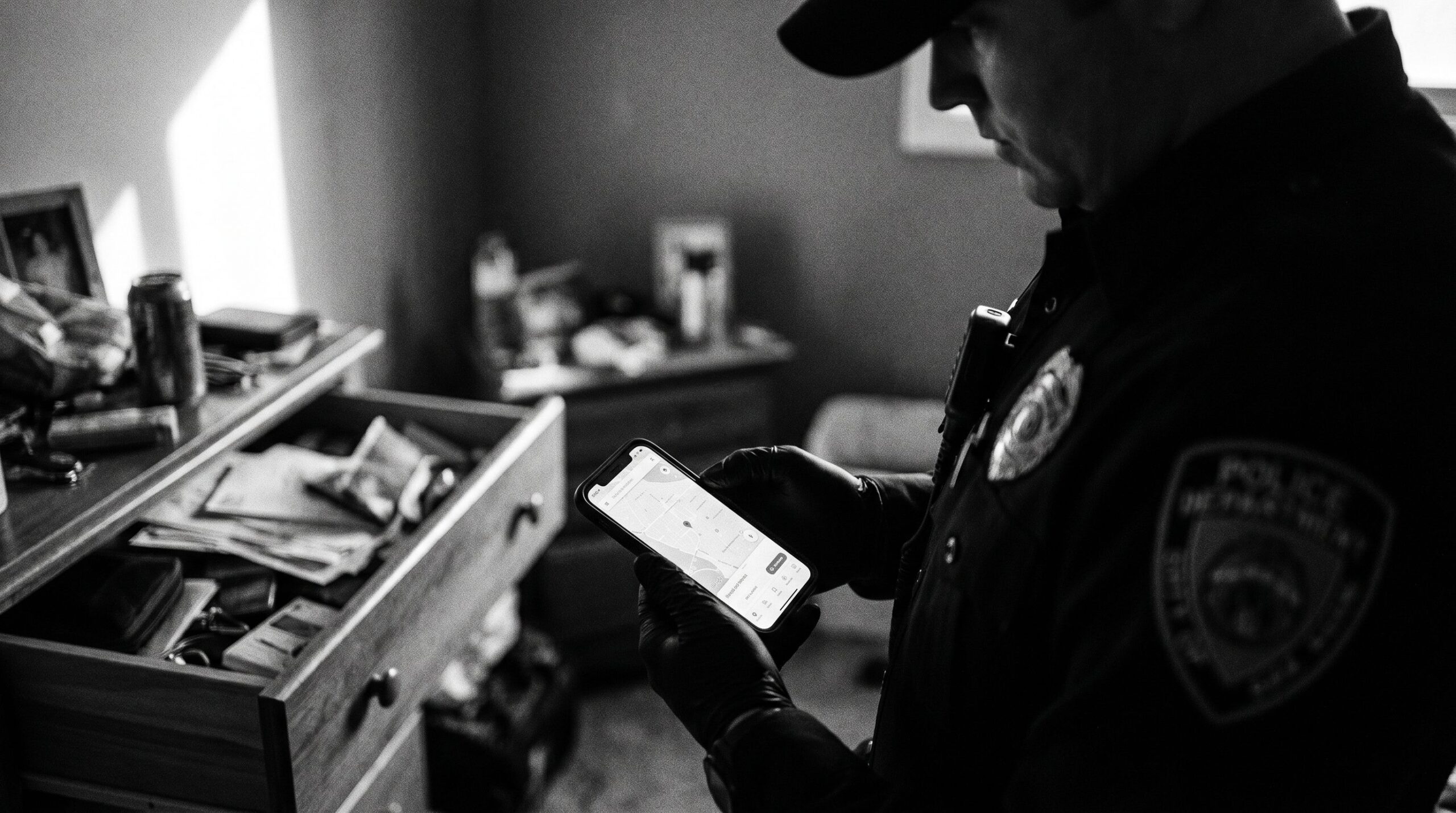 Police officer in uniform holding a seized iPhone during a home search — smartphone seizure and the IT fundamental right