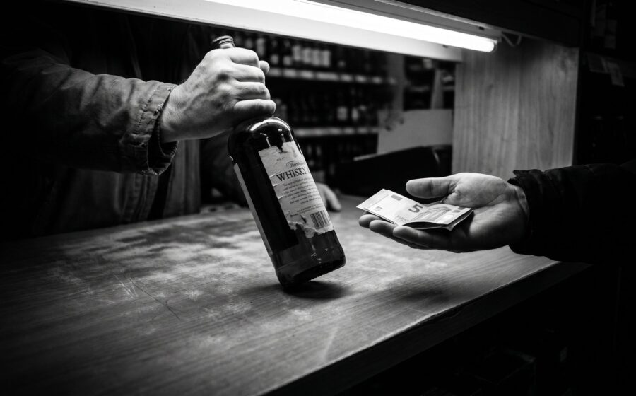 Hands exchanging a whisky bottle for cash at a liquor store counter