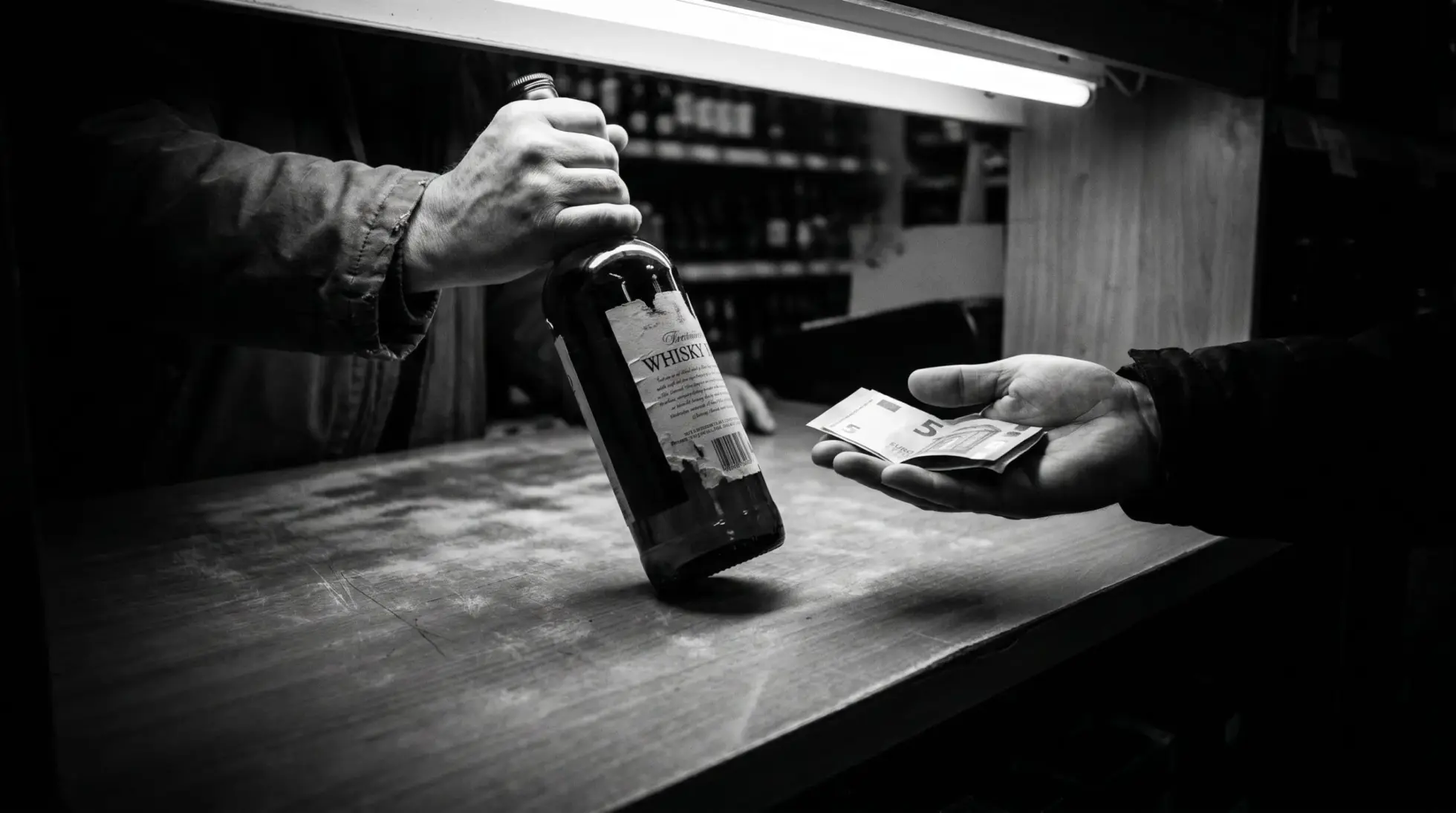 Hands exchanging a whisky bottle for cash at a liquor store counter