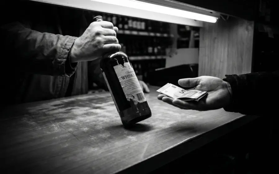 Hands exchanging a whisky bottle for cash at a liquor store counter