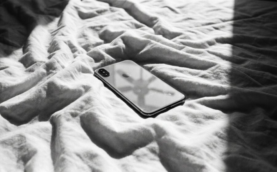 Ein ausgeschaltetes Smartphone liegt mit dem Display nach unten auf einem zerknitterten weissen Bettlaken