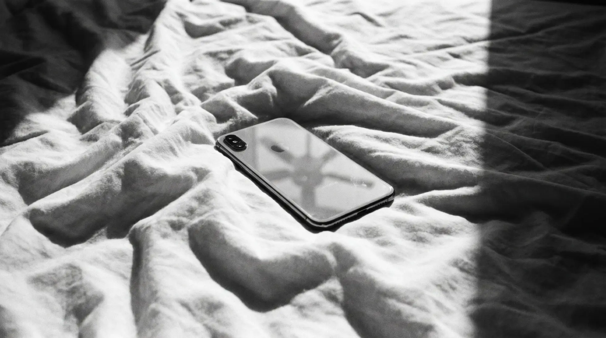 A switched off smartphone lying face down on a crumpled white bed sheet, opening image on 5 days without phone or feed