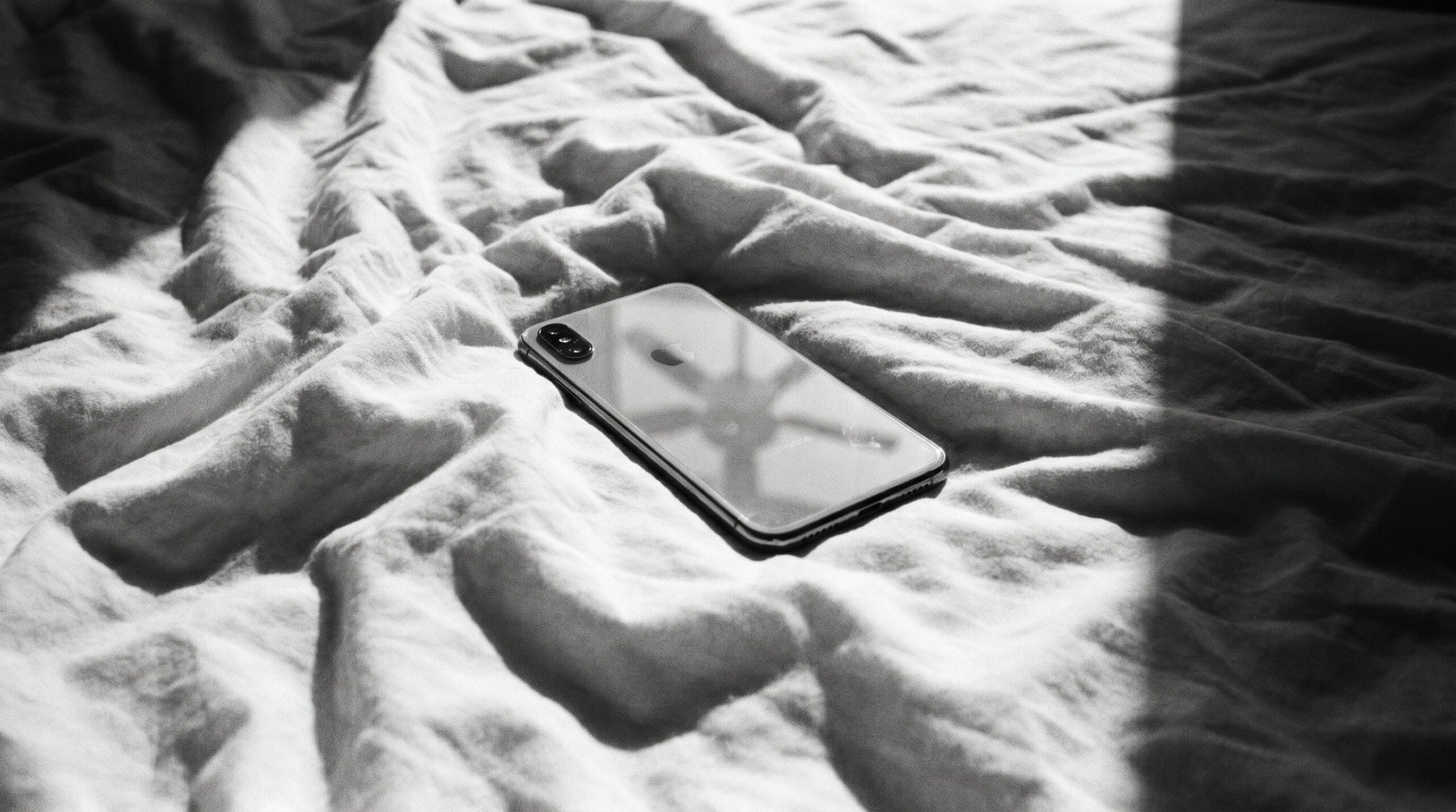 Ein ausgeschaltetes Smartphone liegt mit dem Display nach unten auf einem zerknitterten weissen Bettlaken