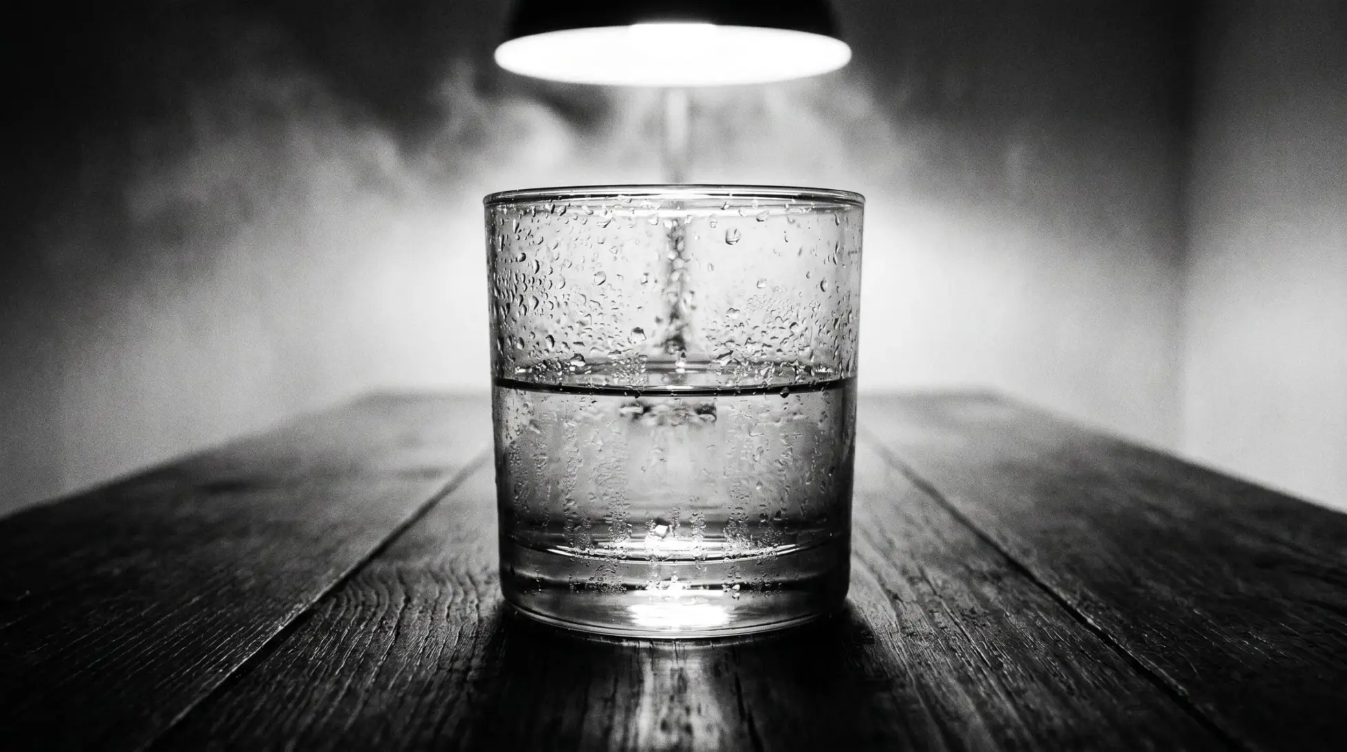 A half full water glass under a hanging lamp on a dark wooden table, on hyponatremia and the balance of water and salt