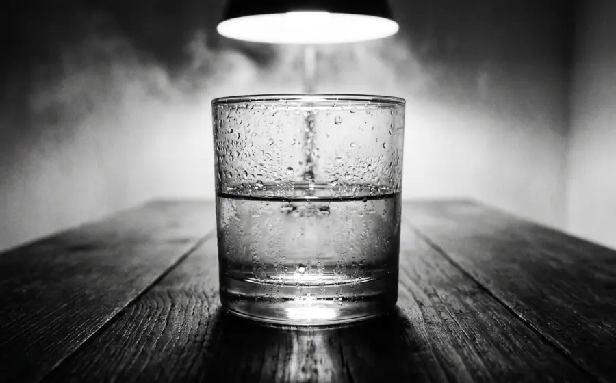 A half full water glass under a hanging lamp on a dark wooden table, on hyponatremia and the balance of water and salt