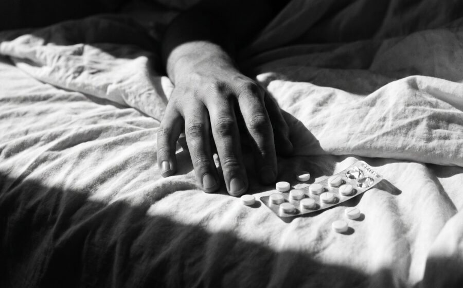 Schwarz-weiss: Hand auf einem Bettlaken neben offenen Tabletten und einer Packung, Rand zu Rand