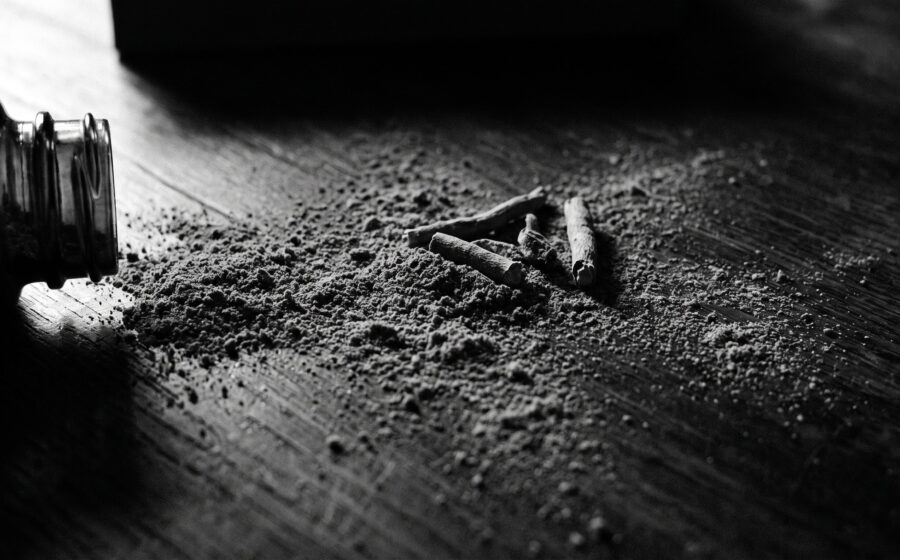 Schwarz-weiss: geoeffnete Ashwagandha-Kapseln und Wurzelpulver auf dunklem Holz, Rand zu Rand