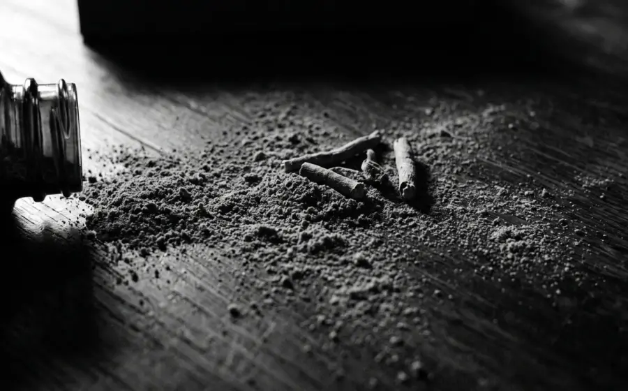 A tipped glass jar spilling ashwagandha root powder and opened capsules across dark wood, on cortisol and chronic stress